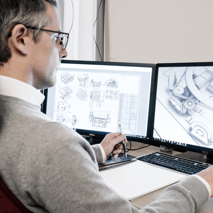 tre män tittar på projicerad bild A man looks at two computer screens with design drawings