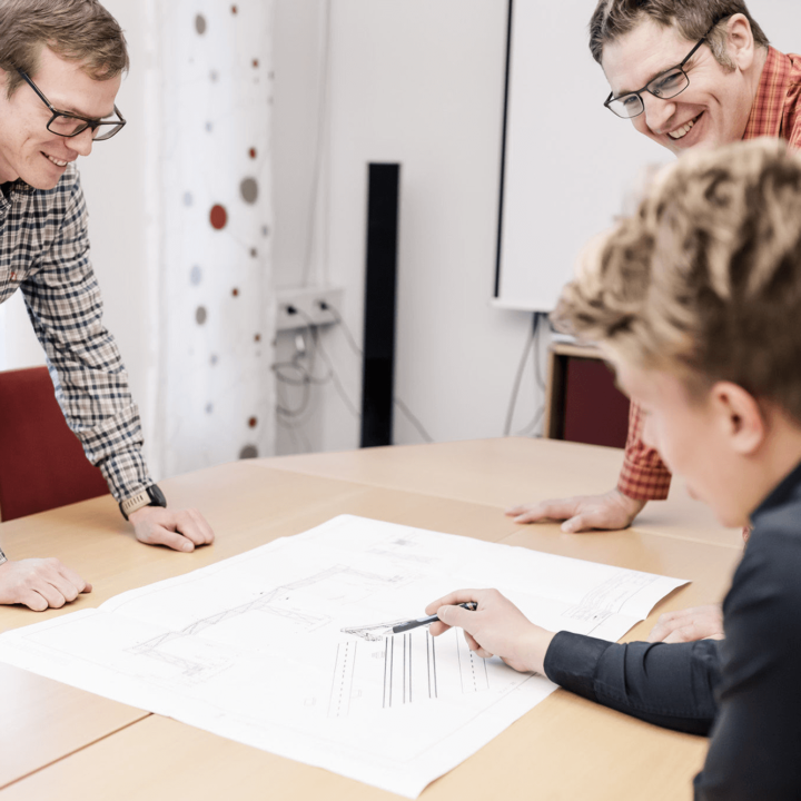 Three men stand at a table on which is a drawing